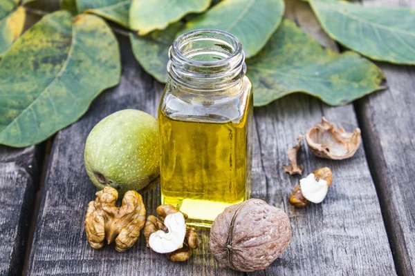 Walnut oil in a glass jar near walnuts and green leaves on a wooden table. — Stockfoto