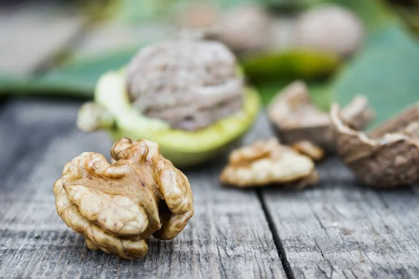 Nueces frescas en una cáscara verde cerca del núcleo de la nuez en una mesa de madera vieja. Nueces en conchas verdes . —  Fotos de Stock