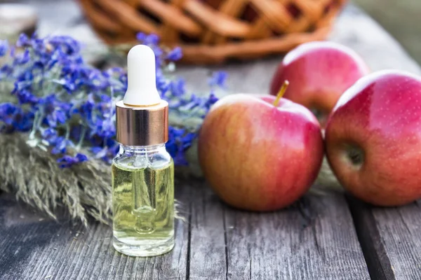 Стеклянная бутылка яблочного эфирного масла возле свежих яблок на деревянном столе. Эфирное масло используется для наполнения светильников, парфюмерии и косметики . — стоковое фото