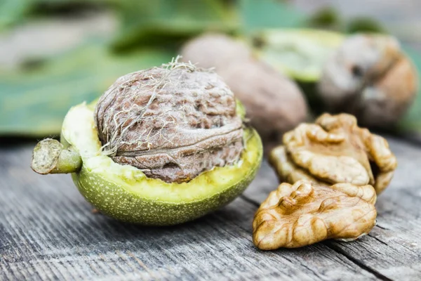 Nueces frescas en una cáscara verde cerca del núcleo de la nuez en una mesa de madera vieja. Nueces en conchas verdes . —  Fotos de Stock