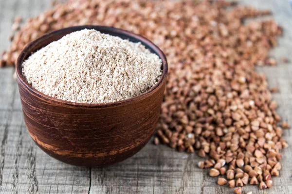 Buckwheat flour in a bowl near the buckwheat grain. A pile of buckwheat flour.