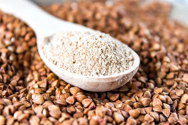 Buckwheat flour in a wooden spoon on a pile of roasted buckwheat. A pile of buckwheat flour.