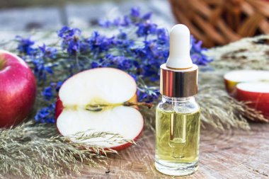 Elma yağı şişesi ve ahşap bir masada taze elmalar. Temel yağ lambaları, parfümleri ve kozmetik ürünlerini doldurmak için kullanılır..
