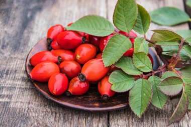 Kırmızı gül kalçalar ve yeşil yapraklar eski ahşap tahtaların üzerinde bir kasede yatıyor..