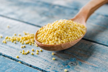 Eski mavi tahtaların arka planına karşı kaşıkta kurumuş sarı darı.