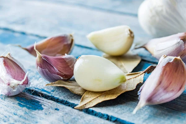 Cloves of garlic and whole garlic near a bay leaf on a blue rustic table.