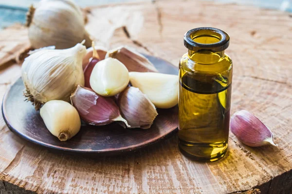 Sarımsak yağı, olgunlaşmış sarımsağın yanındaki cam şişede mavi eski tahtaların arka planında. C