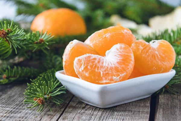 Slices of ripe yellow mandarin lie in a bowl next to the green branches of a Christmas tree. — Stock Photo, Image