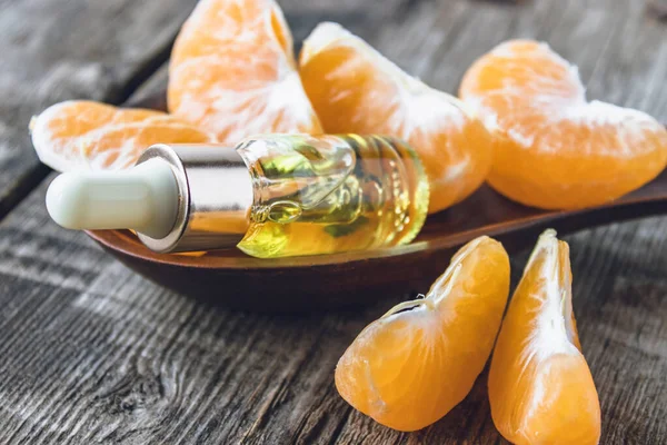Бутылка мандаринского эфирного масла и ломтики спелого желтого мандарина лежат на деревянном столе . — стоковое фото