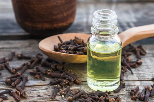 Una botella de aceite esencial de clavo se encuentra cerca de una cuchara con especias de clavo en tablas de madera viejas . — Foto de Stock