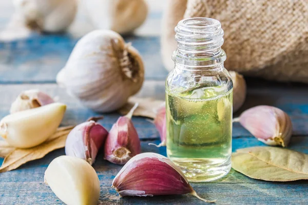 Garlic oil in a glass bottle near ripe garlic on a background of blue old boards. C