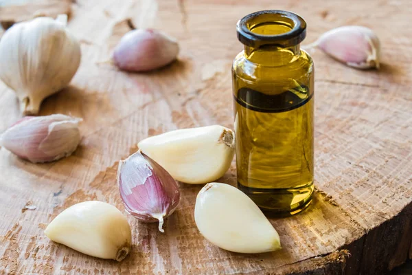 Sarımsak yağı, olgunlaşmış sarımsağın yanında cam bir şişede mavi ahşap bir arka planda..