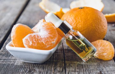 Mandalina yağı, beyaz bir kasenin yanında, içinde mandalina dilimleri olan cam bir şişede..