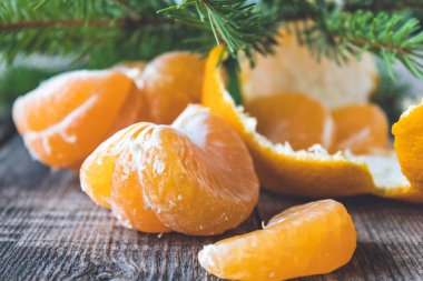 Kabuksuz soyulmuş mandalina ve olgun mandalina dilimleri Noel ağacının yeşil dallarının yanındaki masada..
