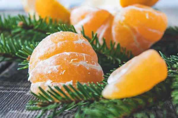 Mandarino sbucciato senza buccia e fette di mandarino maturo sono sul tavolo accanto ai rami verdi dell'albero di Natale . — Foto Stock