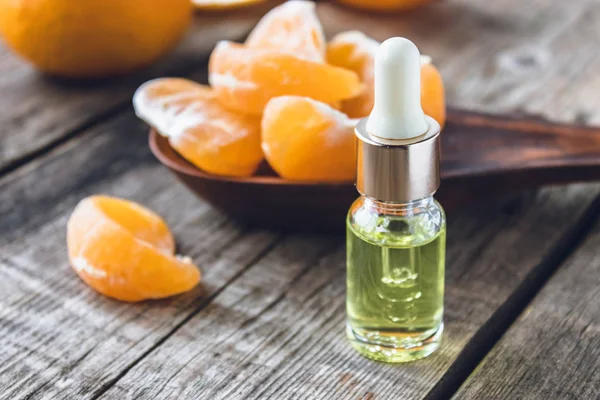 Sebuah botol kaca minyak esensial dengan mandarin dan irisan mandarin matang berada di atas meja . — Stok Foto