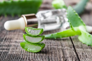 Bir dilim aloe vera ve yeşil yapraklar, ahşap bir masada gerekli olan aloe vera yağı ile..