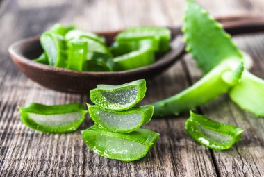 Taze aloe vera yaprakları ve ahşap bir arka planda kaşıkta aloe vera dilimleri..