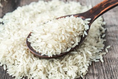 Eski tahtaların arka planına karşı tahta kaşıkla pirinç yığını üzerinde beyaz pirinç. Yasemin pilavı..