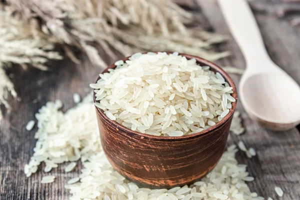 A bowl of white rice next to a pile of rice on a background of old boards. Jasmine rice for cooking.