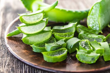 Aloe Vera yaprakları ve aloe dilimleri eski tahtaların arka planında bir kasede.