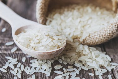 Beyaz pirinç eski tahtaların arka planında bir torbadan yayılmış. Yasemin pilavı..