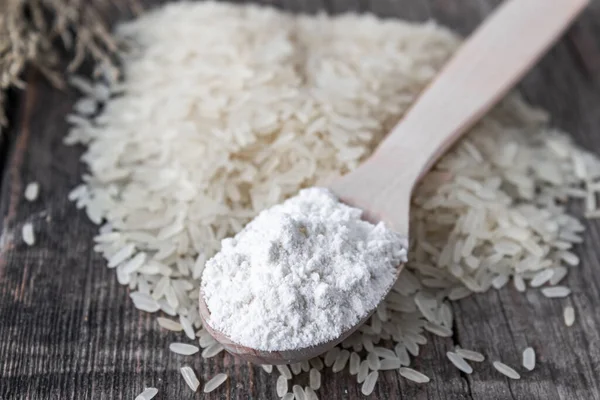 Rice flour in a spoon on a pile of white rice on old boards.