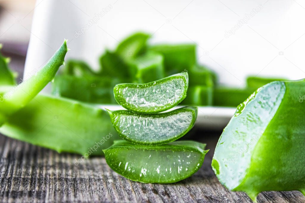 Fresh aloe vera leaves and slices of aloe vera on a wooden background.