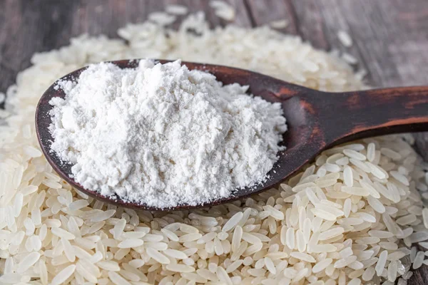 Rice flour in a spoon on a pile of white rice on old boards.