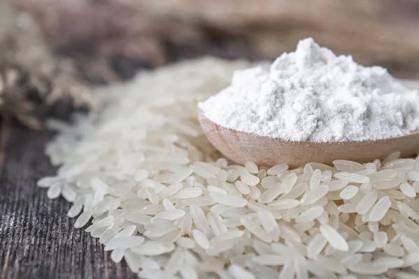 Rice flour in a spoon on a pile of white rice on old boards.