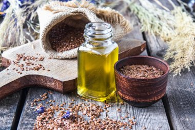 Keten tohumu yağı eski tahtaların arka planında keten tohumlarının yanında bir kavanozda. Keten tohumu yağı yemek, ilaç ve kozmetolojide kullanılır..