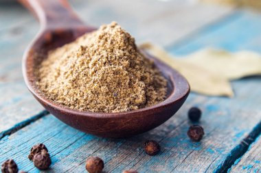 Bir kaşığın içindeki kara biber, mavi panoların arka planında, bezelye ve defne yaprağının yanında yatar. Pişirmek için karabiber ve baharat.