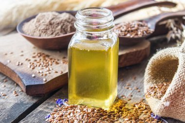 Keten tohumu yağı eski tahtaların arka planında keten tohumlarının yanında bir kavanozda. Keten tohumu yağı yemek, ilaç ve kozmetolojide kullanılır..