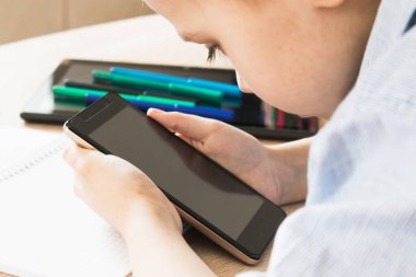 Bir çocuk cep telefonuyla uzaktan öğrenme dersleri alıyor. Uzaklık öğrenme ve çevrimiçi öğrenme kavramı.