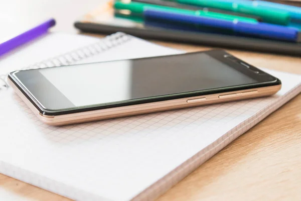 A mobile phone and a notebook are on the table. The concept of distance learning and online learning.