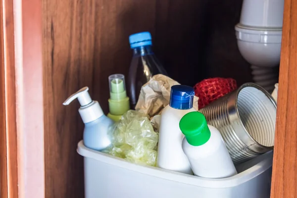 Plastic trash can in the kitchen cabinet - bottles, plastic and metal cans in the trash bin in the kitchen. Garbage waste.