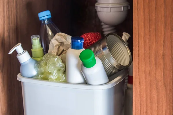 Plastic trash can in the kitchen cabinet - bottles, plastic and metal cans in the trash bin in the kitchen. Garbage waste.