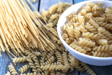 Farklı bir makarna yığınının yanındaki mavi tahtaların arka planında bir kasede kuru makarna. Sağlıklı beslenme ya da sağlıklı yaşam tarzı.