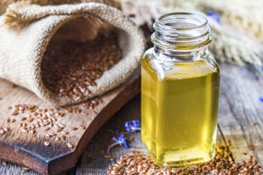 Keten tohumu yağı eski tahtaların arka planında keten tohumlarının yanında bir kavanozda. Keten tohumu yağı yemek, ilaç ve kozmetolojide kullanılır..