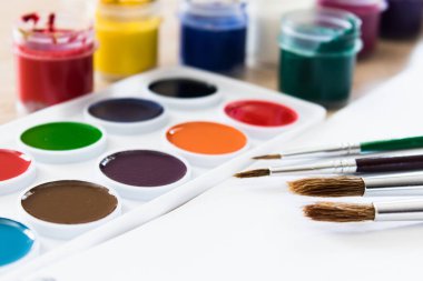 Masanın üzerinde suluboya boyalar, fırçalar ve guaj boyaları var. Çizim, yaratıcılık ve hobiler için hazır. Yakın plan..