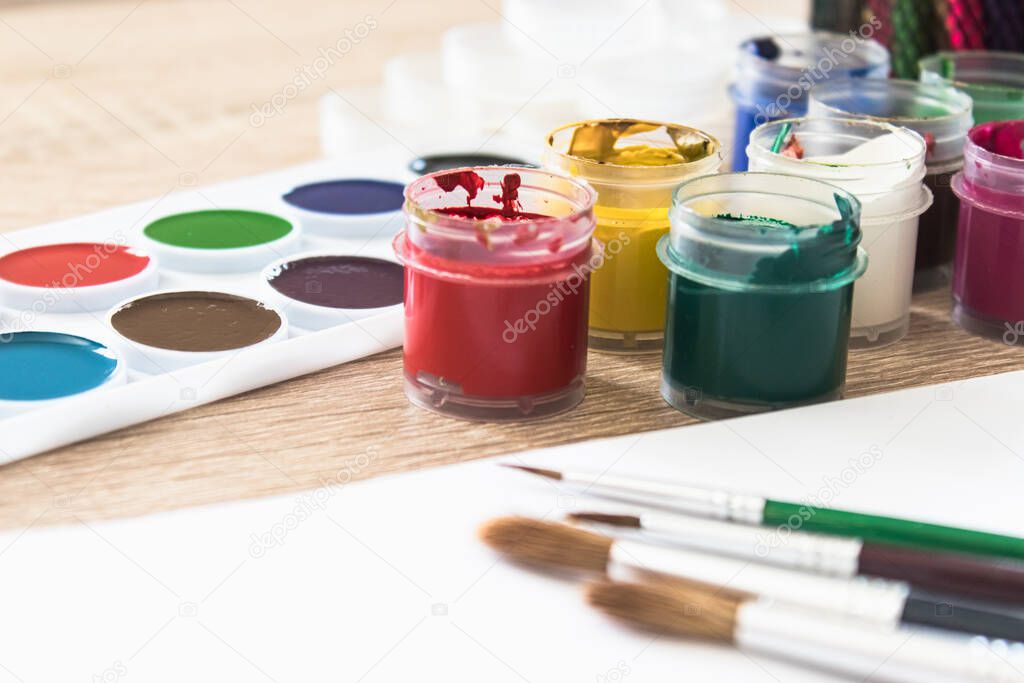 On the table are watercolor paints, brushes and gouache paints. Set for drawing, creativity and hobbies. Close-up.