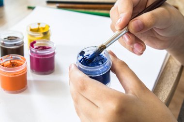 Çocuğun elleri, beyaz arka plandaki bir kutudan gouache çizmek ve çizmek için bir fırça tutuyor. Çocuklar için hobiler ve eğlence. Yakın plan..