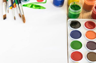 Masanın üzerinde suluboya boyalar, fırçalar ve guaj boyaları var. Çizim, yaratıcılık ve hobiler için hazır. Yakın plan..