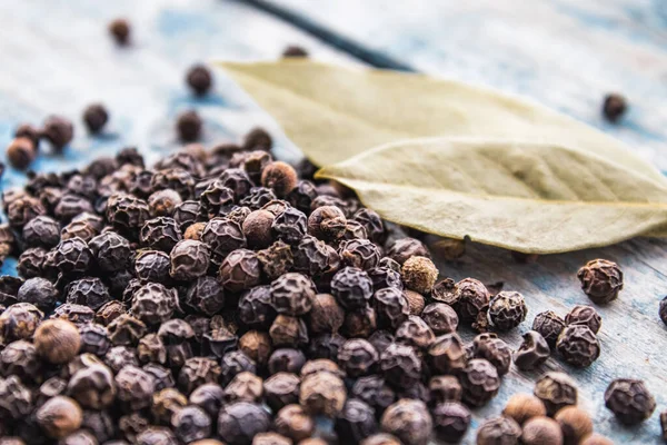 stock image Black pepper and bay leaves are scattered on blue boards. Black pepper spices and seasonings for cooking.