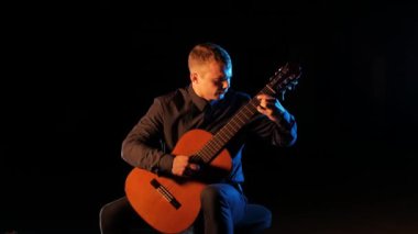 Müzisyen, siyah bir zemin üzerinde akustik bir gitarla klasik müzik çalıyor.