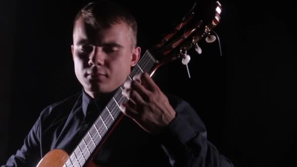 ハンサムな若い男が黒の背景に古典的なアコースティックギターを巧みに演奏し顔の近くに孤立した — ストック動画