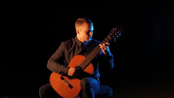 男性の演奏家は黒を基調としたアコースティックギターでクラシック音楽を演奏し — ストック動画
