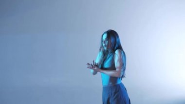 Uzun saçlı, çağdaş dans eden genç ve güzel bir dansçı kız stüdyoda dans ediyor. Renkli arka plan ışığı, yavaş çekim, izole edilmiş, orta boy.