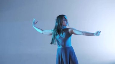 Uzun saçlı, çağdaş dans eden genç ve güzel bir dansçı kız stüdyoda dans ediyor. Renkli arka plan ışığı, yavaş çekim, izole edilmiş, orta boy.