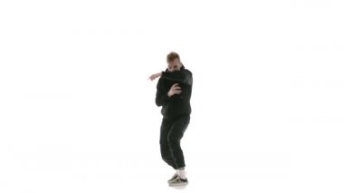Siyah eşofmanlı genç yakışıklı adam güçlü bir şekilde hip hop, serbest stil, sokak dansı yapıyor. Karmaşık hareketler yapıyor.
